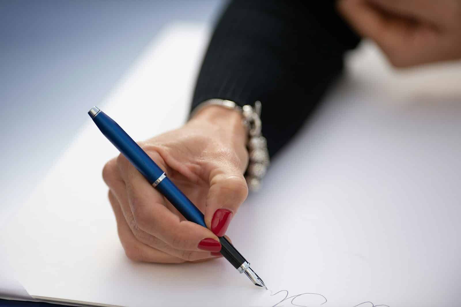 A hand writing with a blue pen on paper.