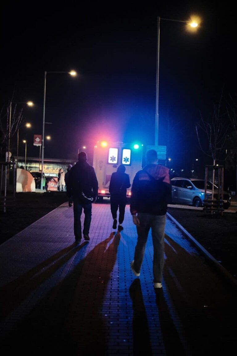 People walk towards an ambulance at night.