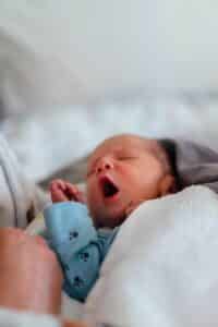 baby in white and blue onesie lying on bed